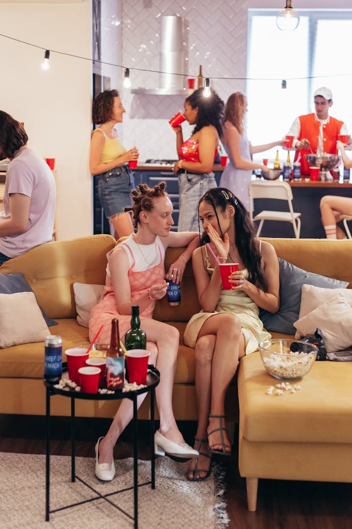 Group of friends enjoying a lively indoor gathering with drinks and conversation on a cozy sofa.